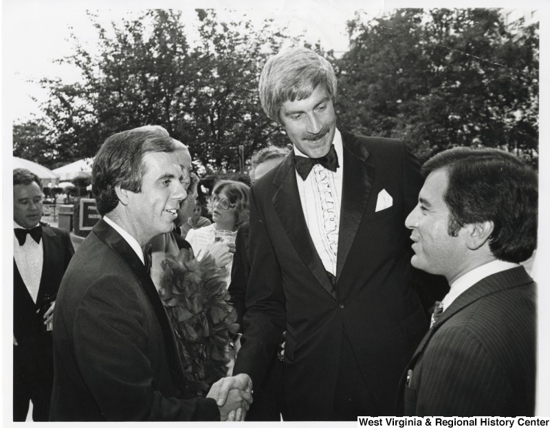Congressman Tony Coehlo (D-CA) shaking the hand of Congressman Tom McMillen (D-MD), former Pro-Basketball star, at the Democratic Congressional Dinner. Congressman Nick Rahall II (D-WV) is standing beside McMillen. Rahall worked in the Democratic cloak room with McMillen.